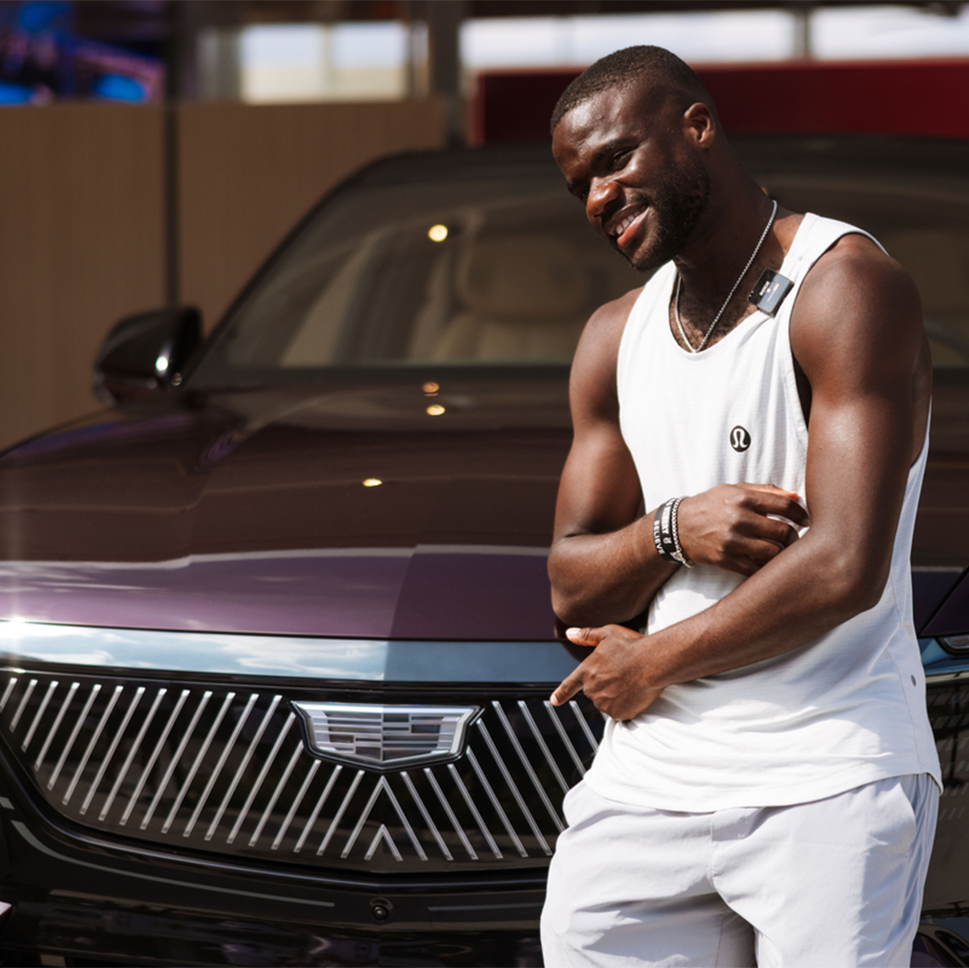 Frances Tiafoe Smiling and Posing in Front of a Dark Purple Cadillac SUV with the Cadillac Grille Prominently Displayed