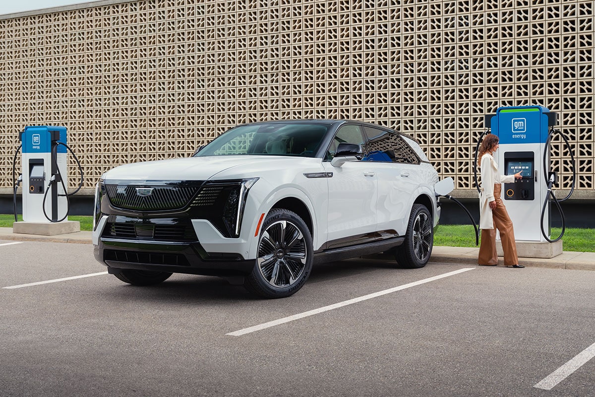 A Woman Getting Ready to Charge a Parked White Cadillac ESCALADE IQ at a GM Energy EV Charger