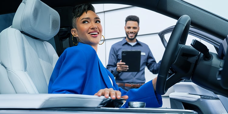 A Smiling Cadillac Customer Sitting in Her Vehicle with a Certified Service Technician Nearby