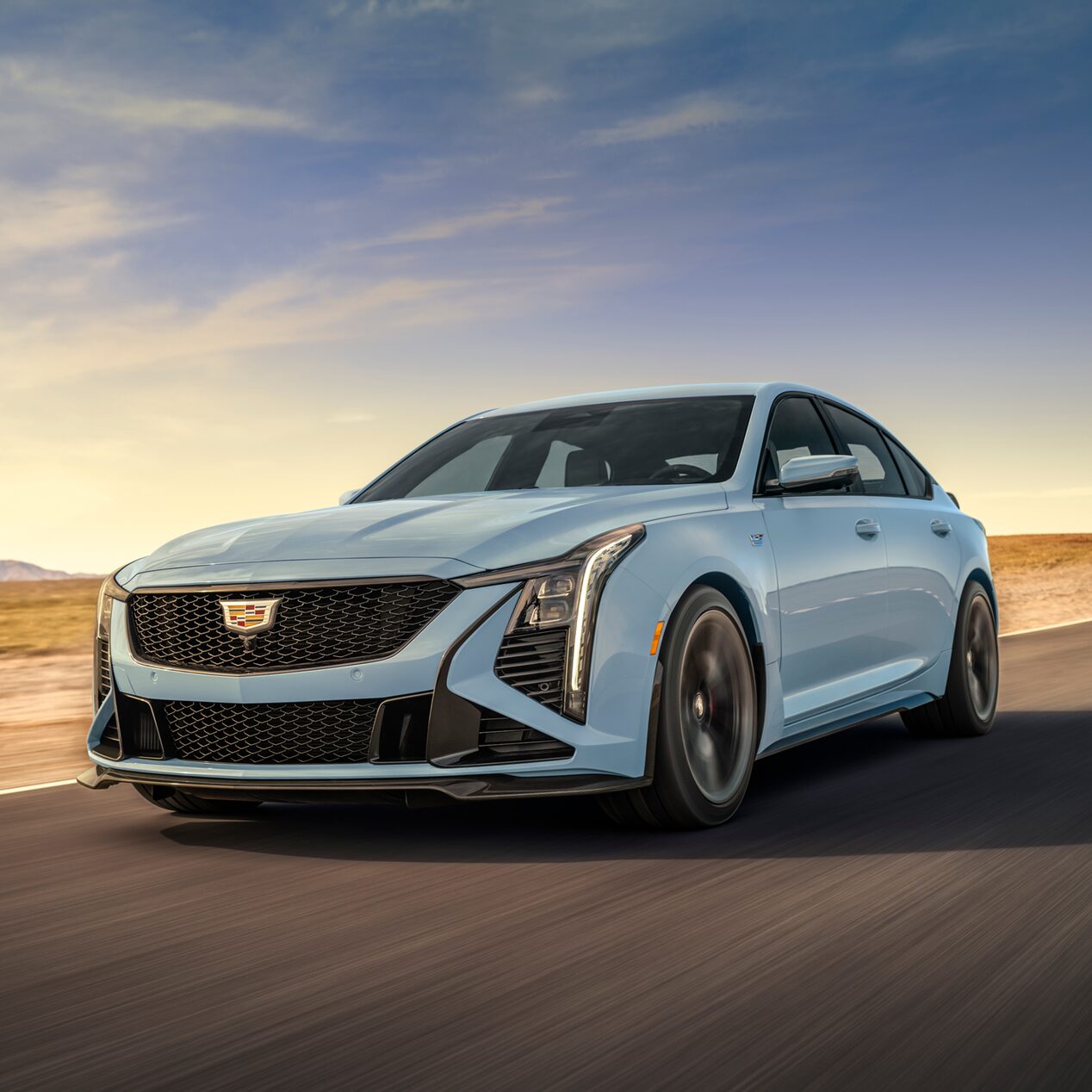 Low Three-Quarters View of a Light Blue 2025 Cadillac CT5-V Driving Down the Road Surrounded by Desert