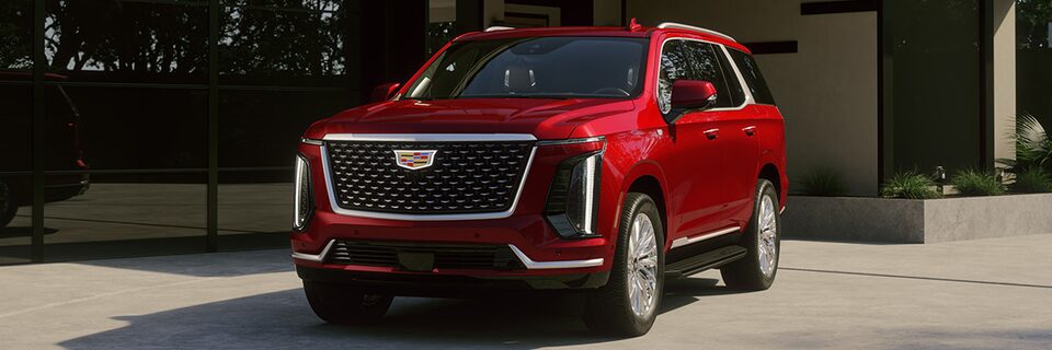 Three-quarter Driver's Side View of a Red Cadillac Escalade Parked Outside of a Modern Home