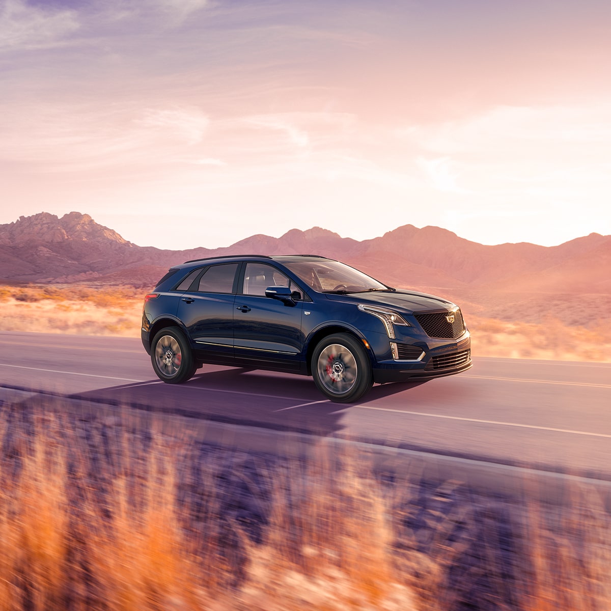 Dark Blue 2025 Cadillac XT5 Driving Down a Western Road at During Golden Hour