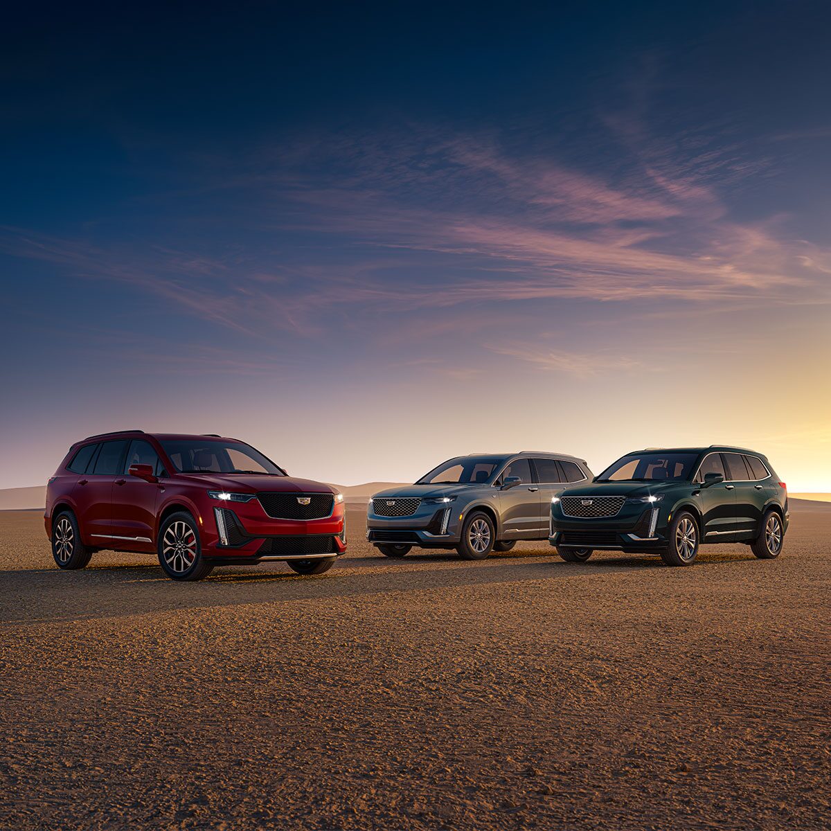 Three Quarters View of Red, Silver and Dark Green Cadillac XT6s Facing Different Directions in a Desert