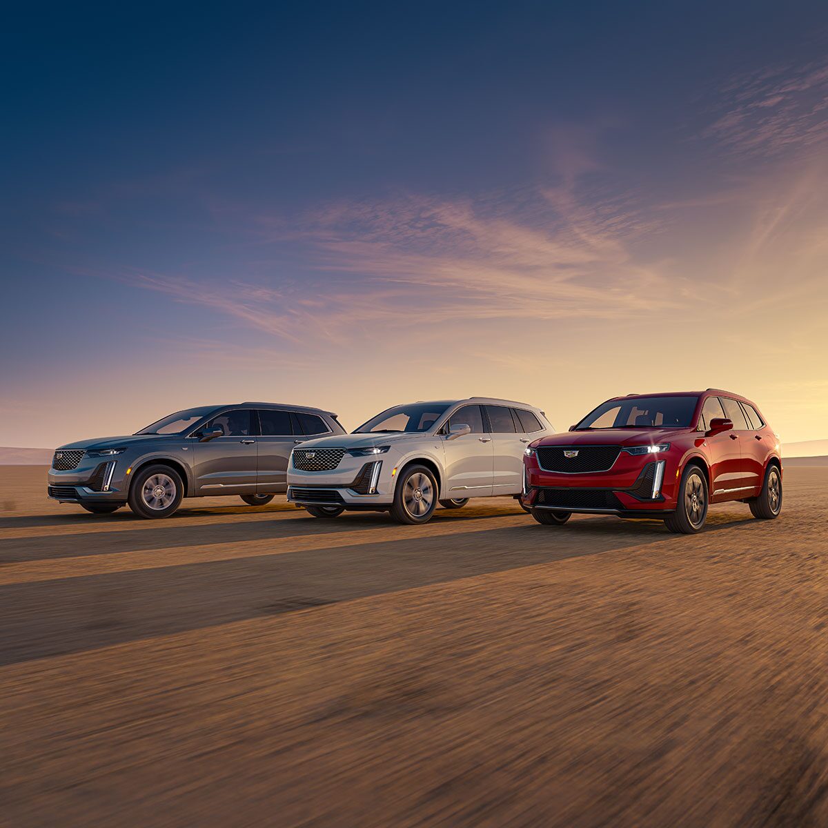 Three Quarters View of Silver, White and Red Cadillac XT6s Parked with a Sunset in the Distance