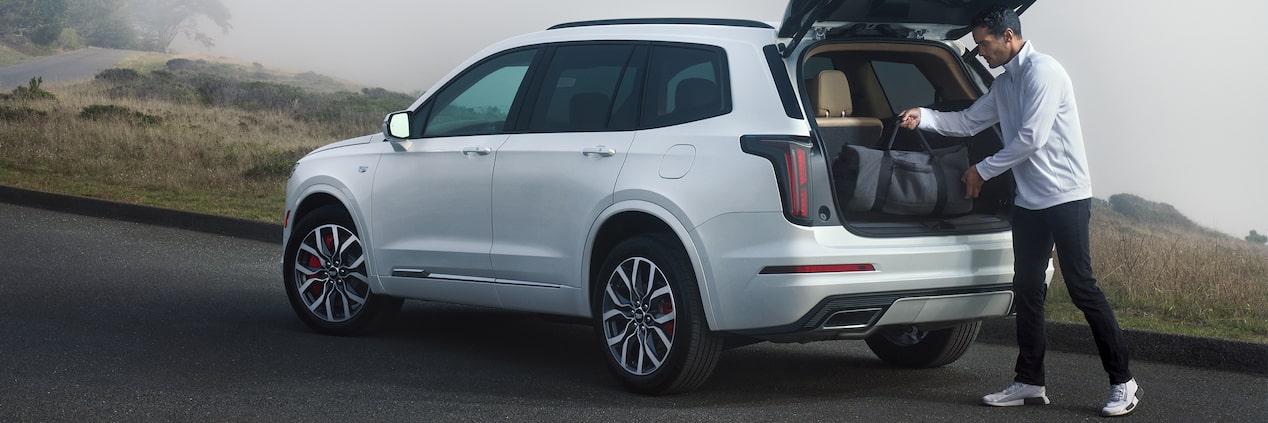 A Man Unloads Cargo from the Trunk of His Cadillac XT6 with Thick Fog in the Distance