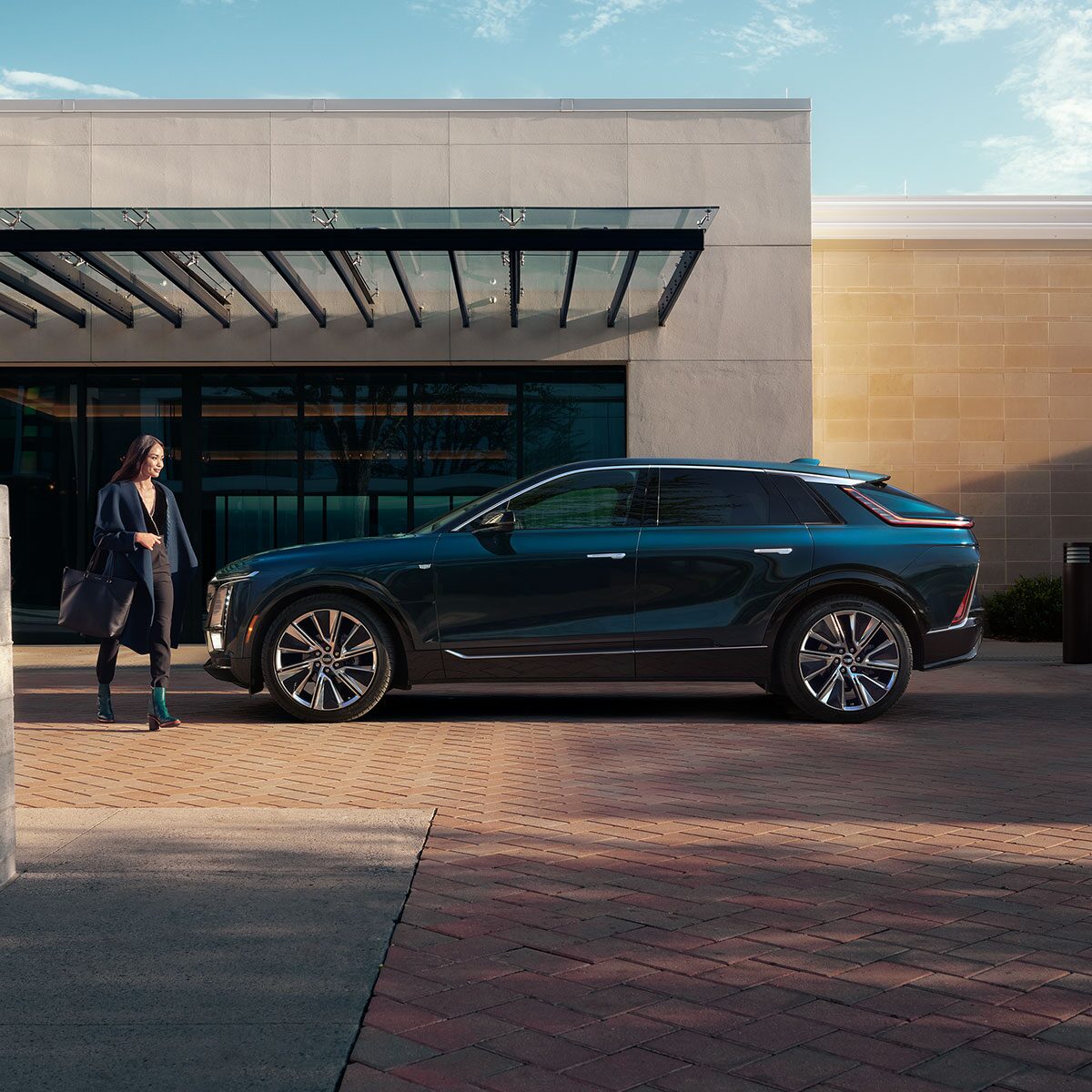 A Woman Walking to the Side Profile of a 2025 Cadillac LYRIQ Parked Outside of a Home