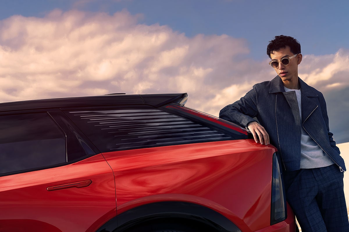A Man in Sunglasses Leaning on the Rear End of a Red 2025 Cadillac OPTIQ