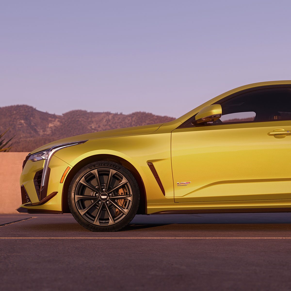 The Front Half Side Profile of a Yellow 2025 CT4-V Driving Past Mountains