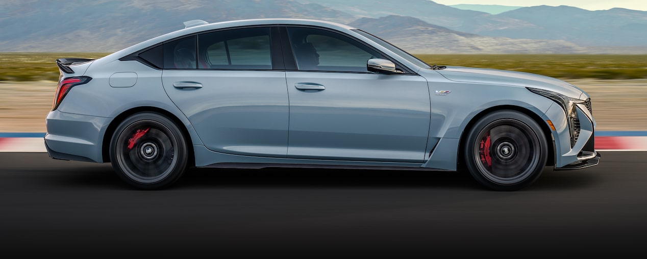 Side View of a Light Blue 2025 Cadillac CT5-V Driving Down the Road with Mountains Visible in the Distance