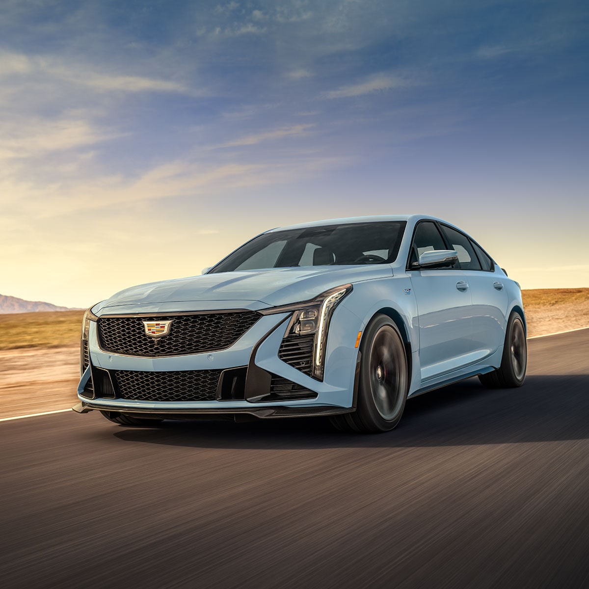 Low Three-Quarters View of a Light Blue 2025 Cadillac CT5-V Driving Down the Road Surrounded by Desert
