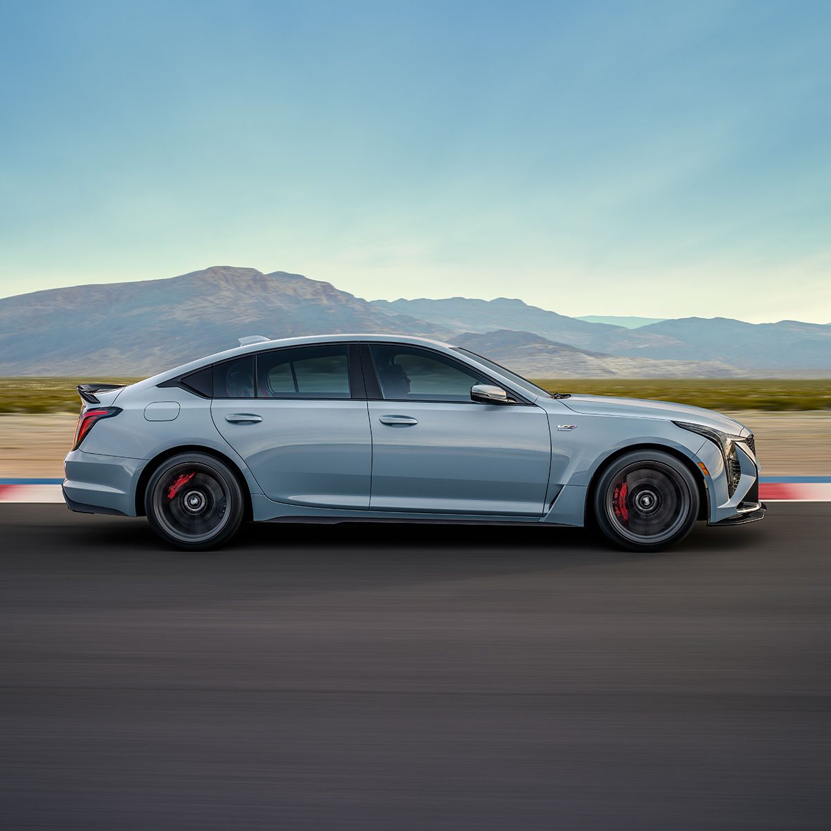 Side View of a Light Blue 2025 Cadillac CT5-V Driving Down the Road with Mountains Visible in the Distance