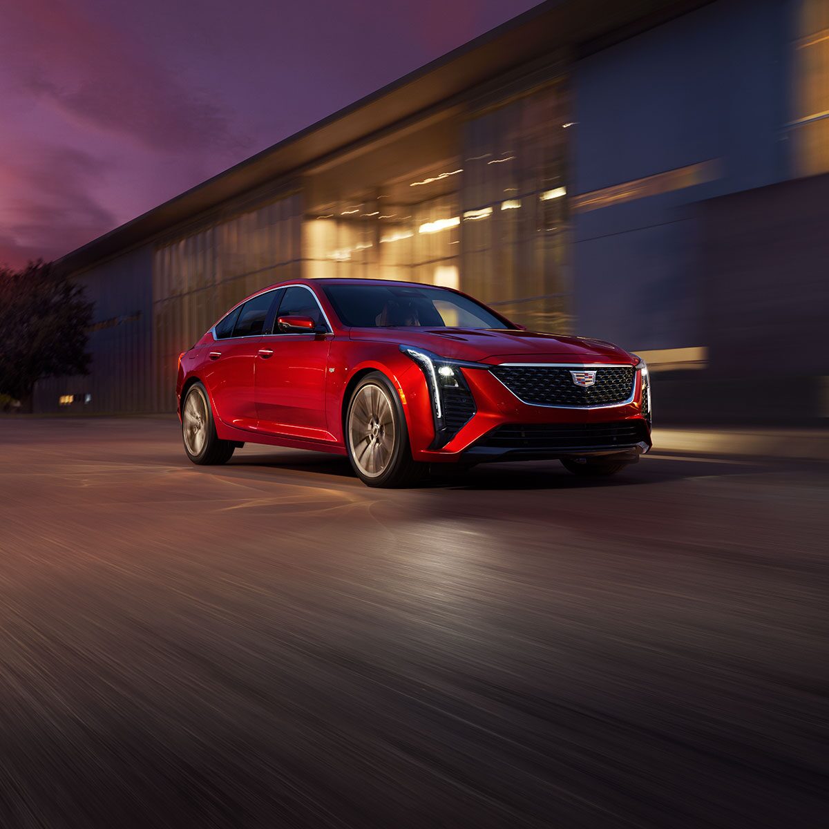 Front View of Red 2025 Cadillac CT5 Driving Past an Industrial Building