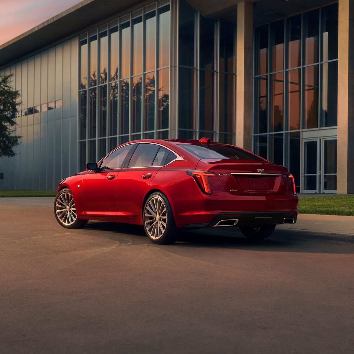 A Driver Side Rear View of a Red 2025 Cadillac Parked Near an Industrial Building
