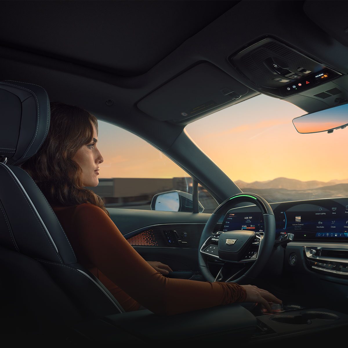 Passenger View of a Woman Utilizing Hands-free Super Cruise Technology Driving the Cadillac LYRIQ During a Sunset