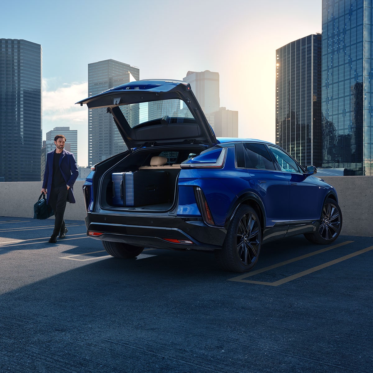 A Man Walking to an Opened Trunk of a Parked Blue Cadillac LYRIQ Overlooking the City