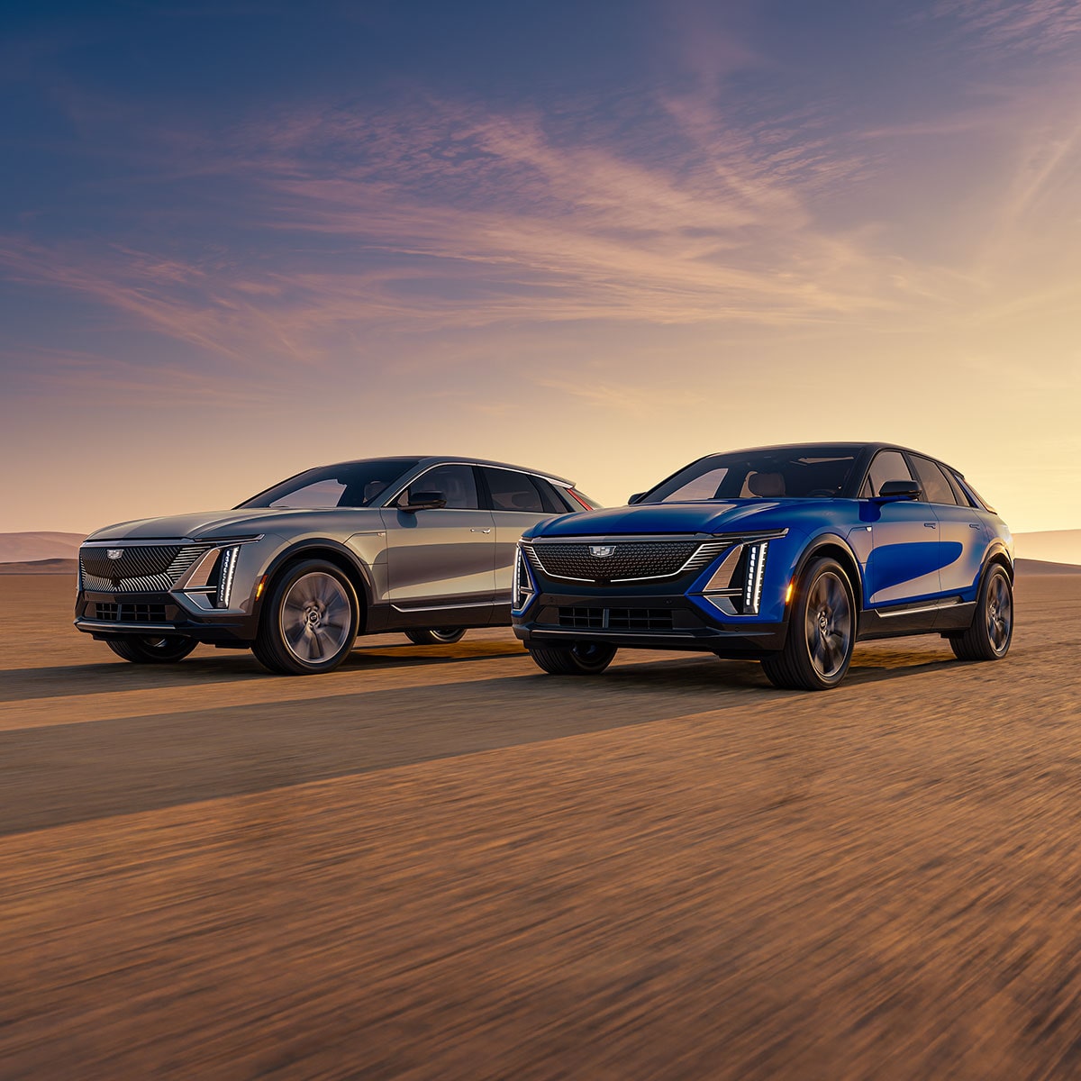 A Blue Cadillac LYRIQ and Silver LYRIQ Parked Next to Each Other in the Desert During a Sunset