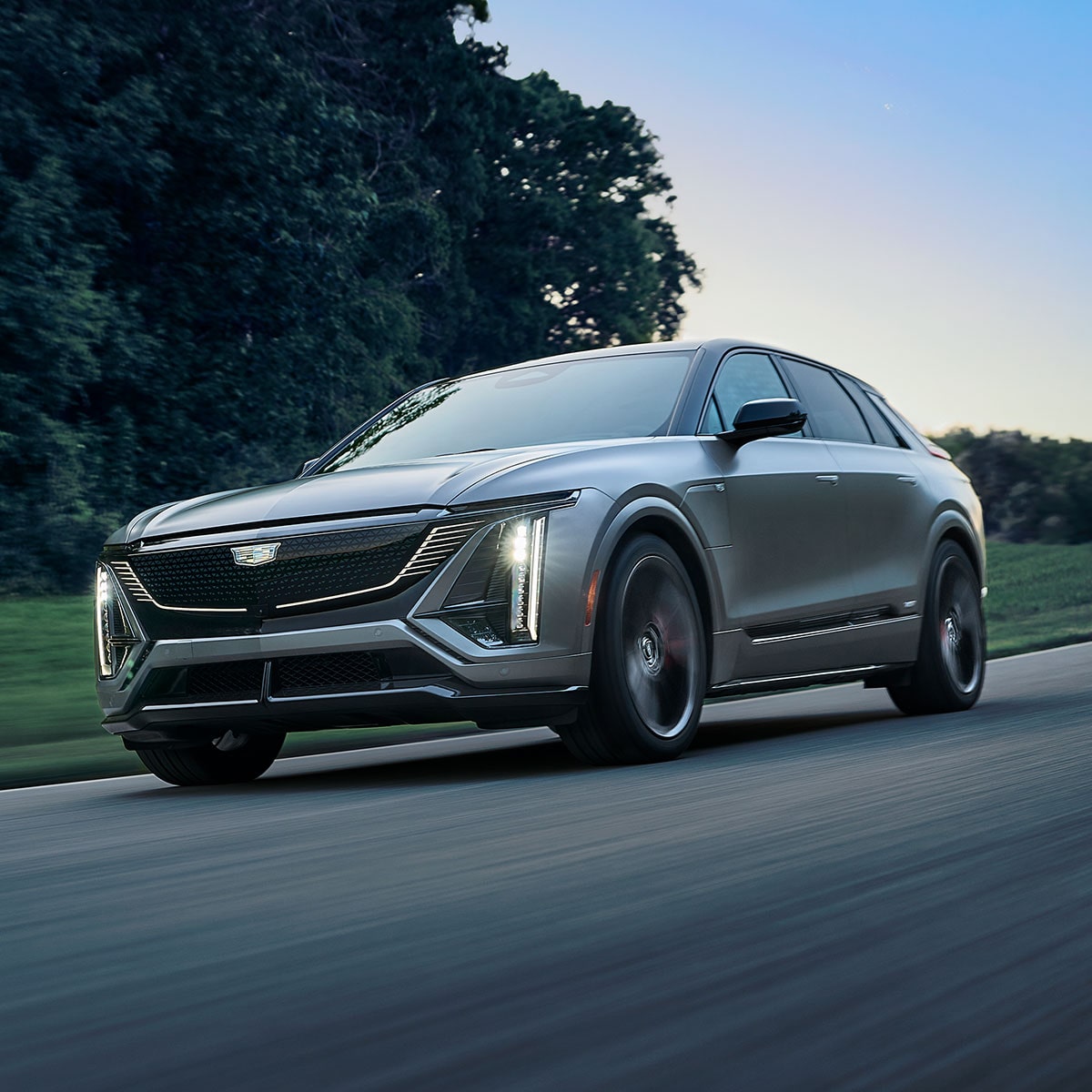 A Silver Cadillac LYRIQ V-Series Luxury Sport SUV Driving During Dusk