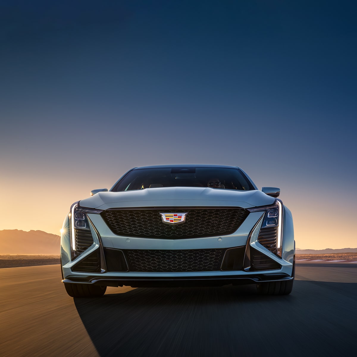 Low Front View of a Light Blue Cadillac CT5-V Driving Down the Road During a Setting Sun