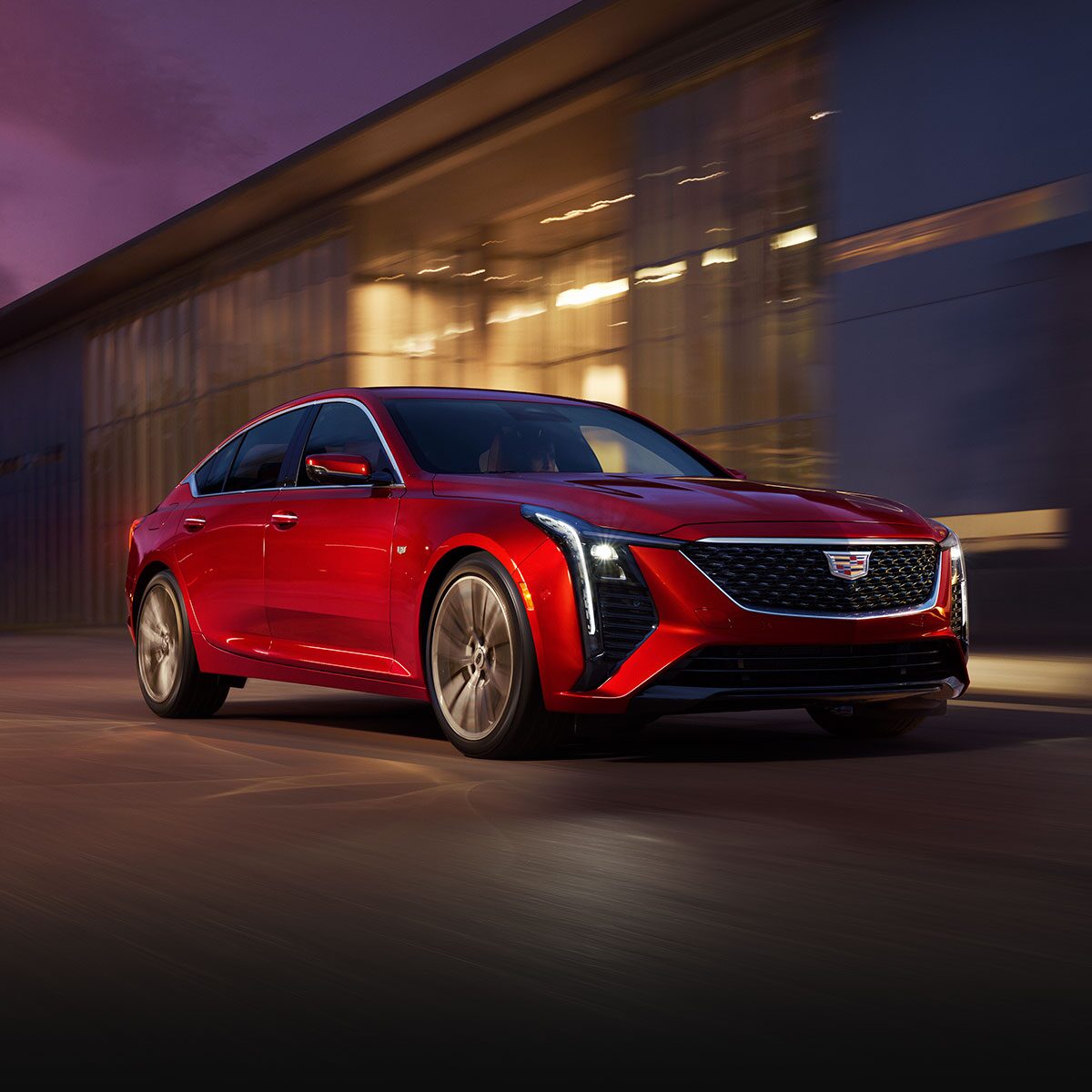 Front View of Red 2026 Cadillac CT5 Driving Past an Industrial Building
