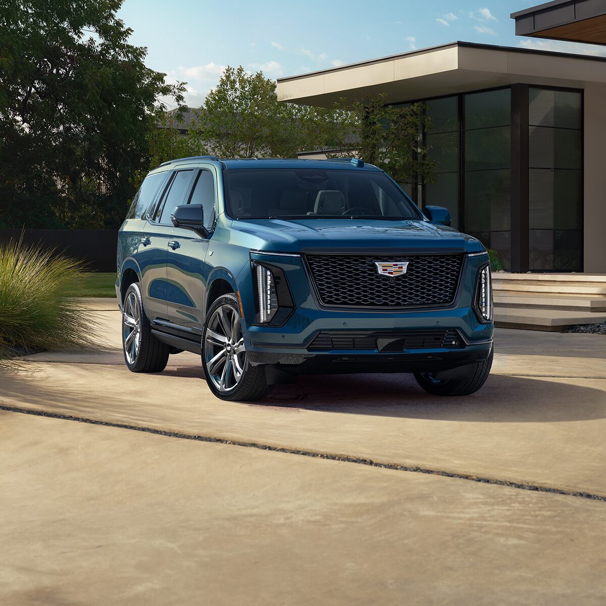 Three-Quarter View of a Blue 2026 Cadillac Escalade Parked in Front of a Modern Home