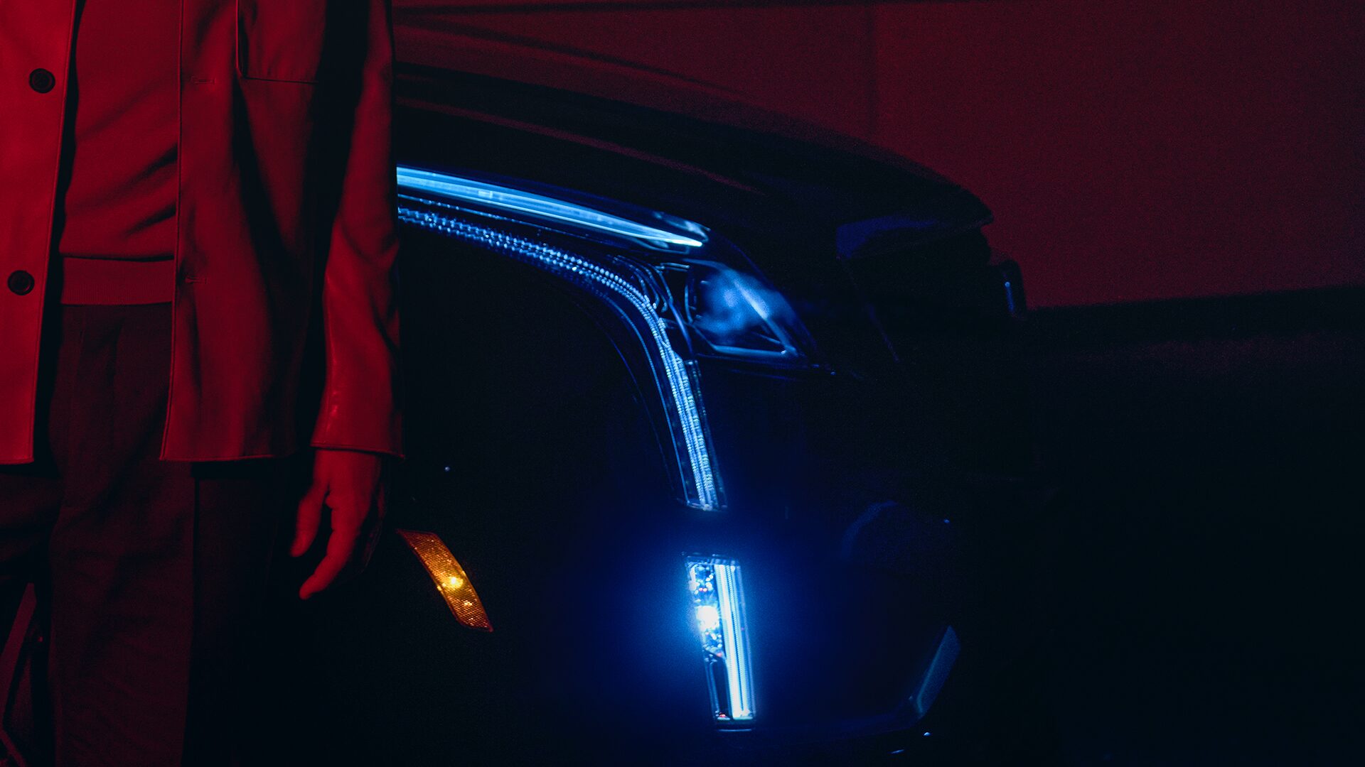 A Man Stands Next to His Cadillac XT5 at Night With Headlamps On