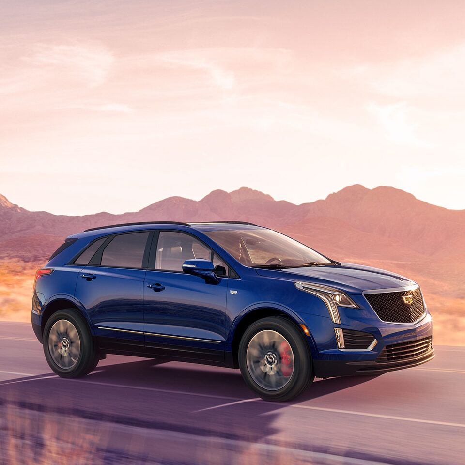 Dark Blue 2026 Cadillac XT5 Driving Down a Western Road at During Golden Hour