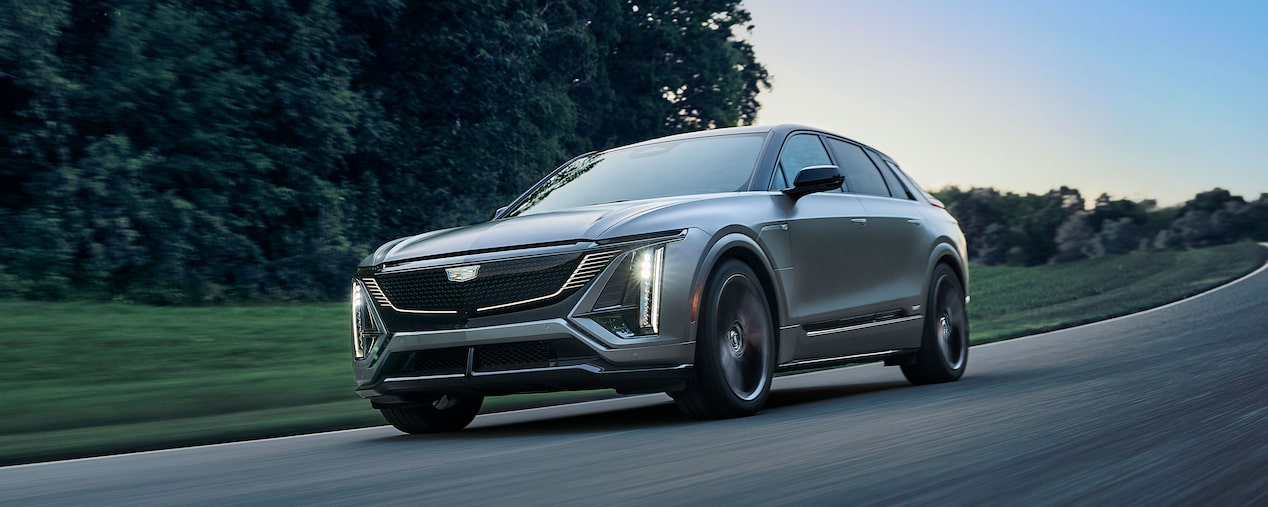A Cadillac V-Series Vehicles Driving Around a Corner on a Road with Trees in the Background