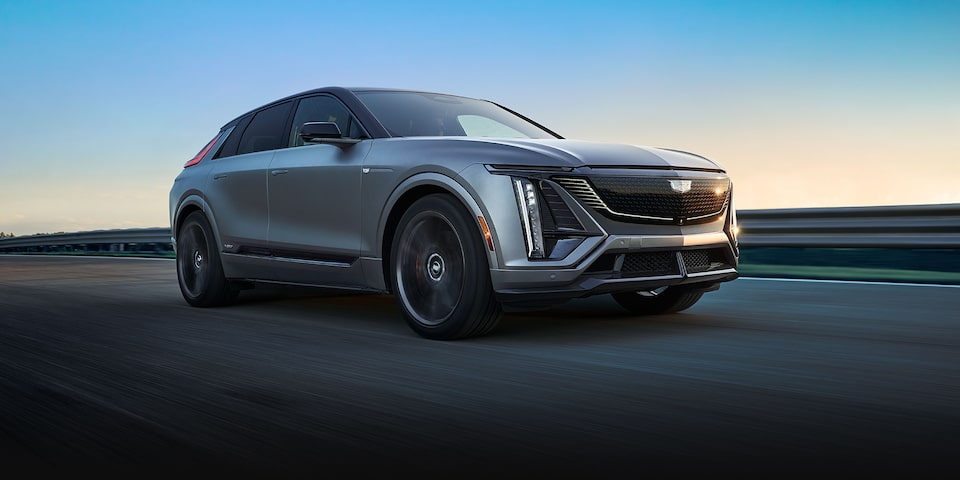 A Silver Cadillac LYRIQ-V Driving Down a Highway with a Clear Blue Sky in the Background