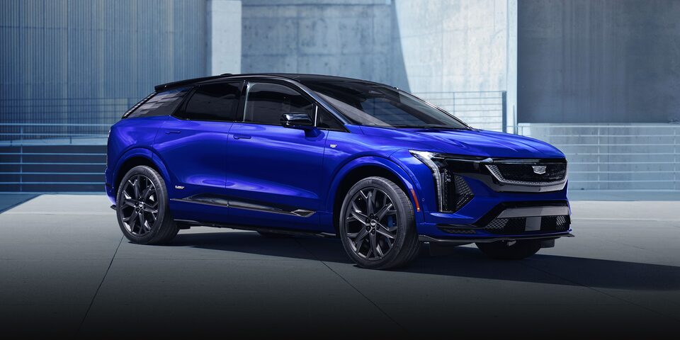 A Blue Cadillac OPTIQ-V Parked in Front of a Grey Wall.